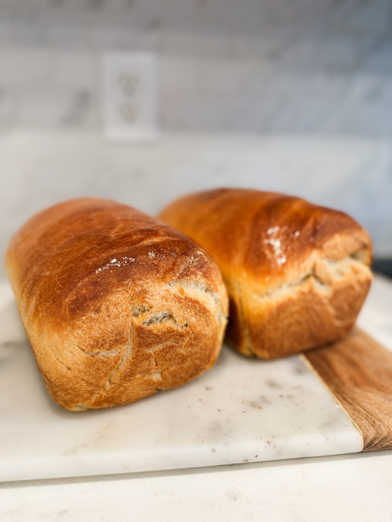 Two golden sourdough sandwich loaves on a marble board